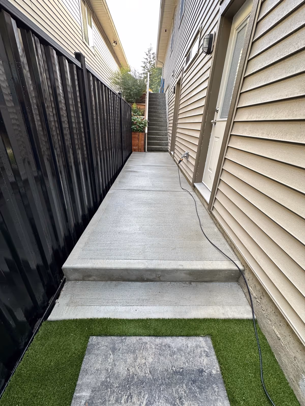 Black metal fence with concrete steps and artificial turf