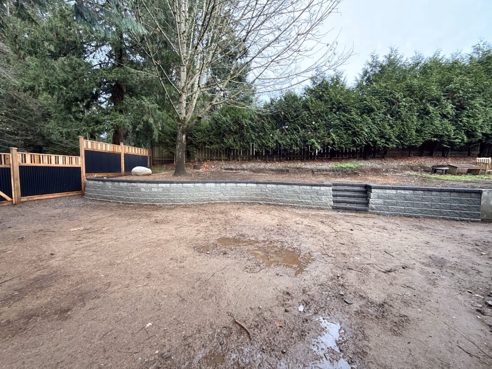 Dark block retaining wall under construction with a fence